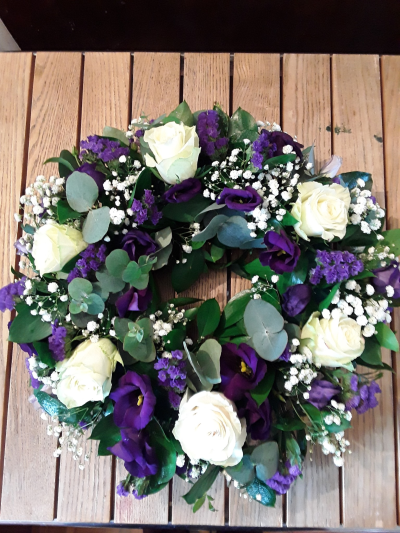 Twilight Wreath - A graceful funeral wreath featuring elegant ivory and deep violet tones blended with soft textures and fresh greenery. Symbolising peace, dignity, and everlasting remembrance, this circular tribute offers a heartfelt expression of sympathy and love for someone dearly missed.