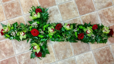 Cross - A striking cross-shaped funeral tribute designed with rich crimson, soft green, and fresh white tones amongst lush foliage. Symbolising faith, love, and eternal remembrance, this elegant arrangement offers a meaningful and heartfelt farewell in honour of a cherished loved one.